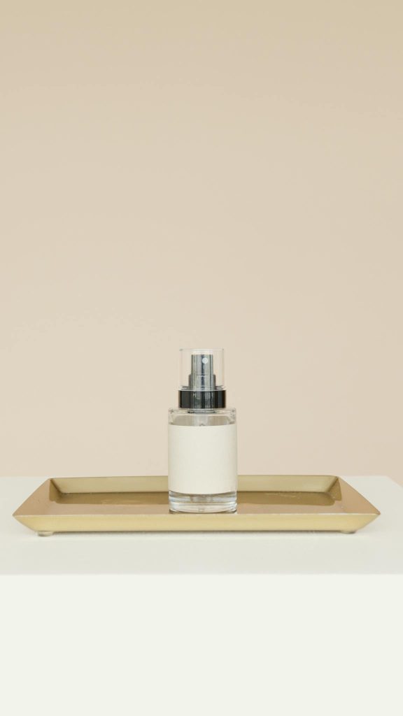 Elegant moisturizer in a glass dispenser placed on a gold tray against a beige backdrop.